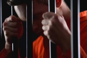 Man in orange jumpsuit cries in a jail cell; Fort Lauderdale defense lawyers fight against evidence-based sentencing that can be discriminatory